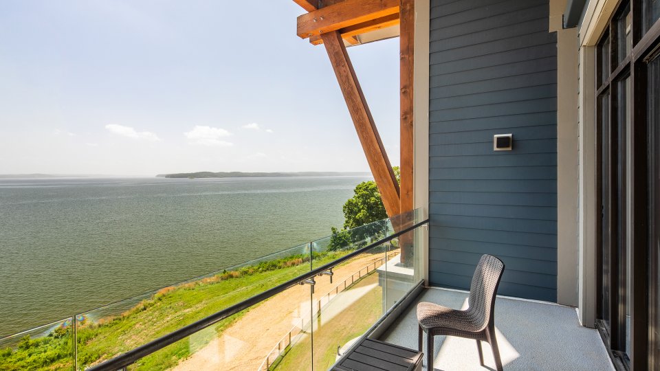 Balcony with chairs overlooking a serene lake and clear blue sky.
