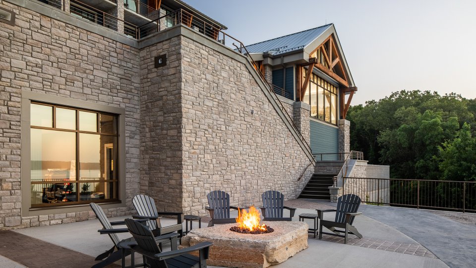 Stone patio with fire pit and chairs, evening light reflecting off the building.
