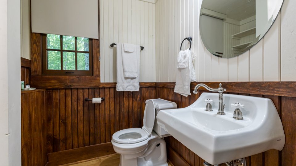 Bathroom with white sink, toilet, wood paneling, and a window above the towel rack.