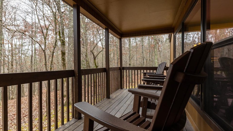 A wooden deck faces the woods with wooden chairs.