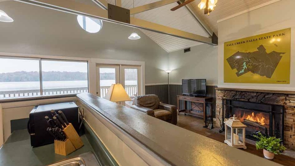 A vaulted ceiling living room features a lit fire place and large windows and doors to the balcony.