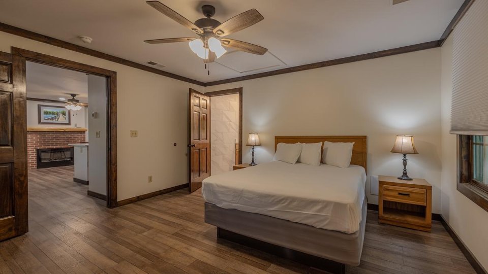 Cozy cabin bedroom with a bed, side table, lamp, and ceiling fan.