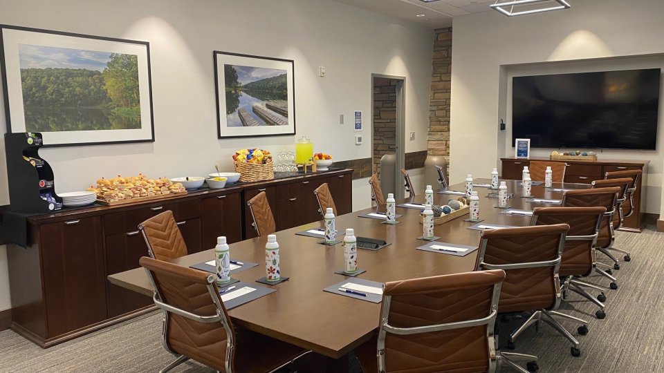Modern boardroom arranged for a meeting with leather chairs, reusable Tennessee State Parks water bottles, and meeting materials at each seat. A refreshment station with sandwiches, snacks, fruit, and beverages lines the back wall beneath framed landscape photos.
