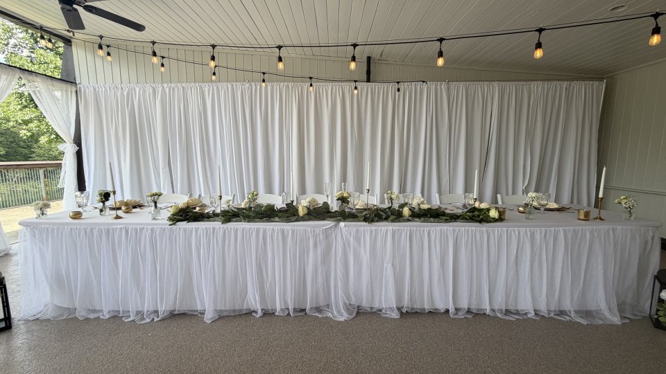 Elegant buffet table setup with white linens and floral decorations under festoon lights.