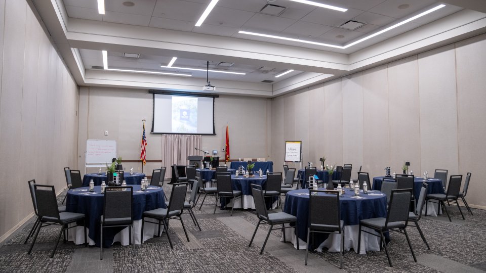 Empty conference room with round tables, blue tablecloths, and presentation screen.