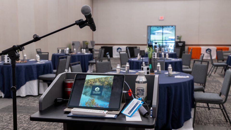 Conference room setup with podium, microphone, and a laptop displaying a presentation.