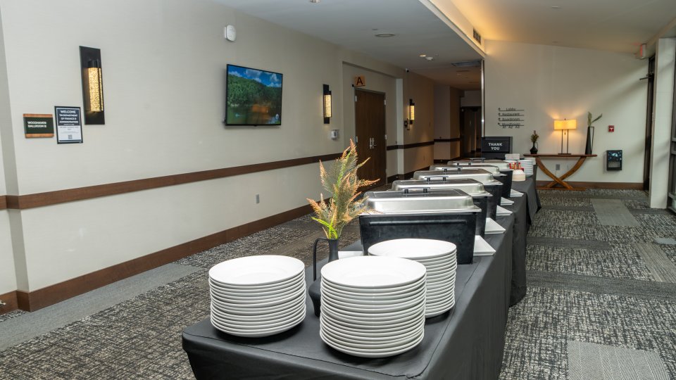 Row of buffet stations with stacks of white plates in a carpeted hallway.