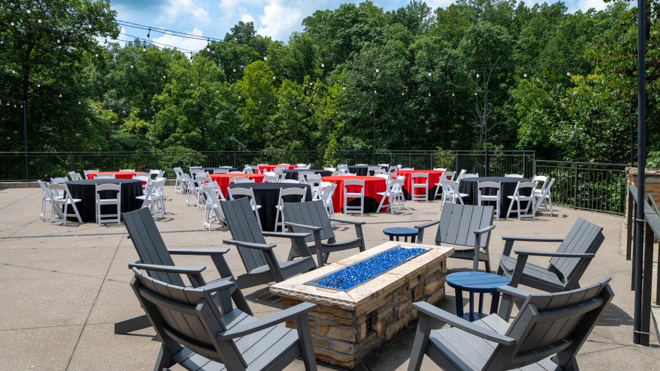 Outdoor patio with grey chairs and fire pit, surrounded by greenery.