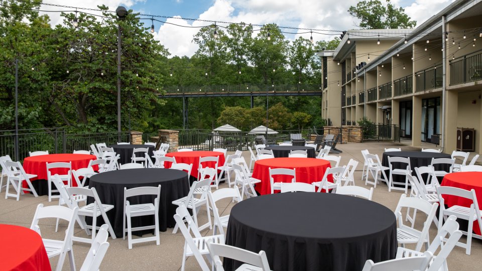 Outdoor event space with black and red tablecloths on white chairs.