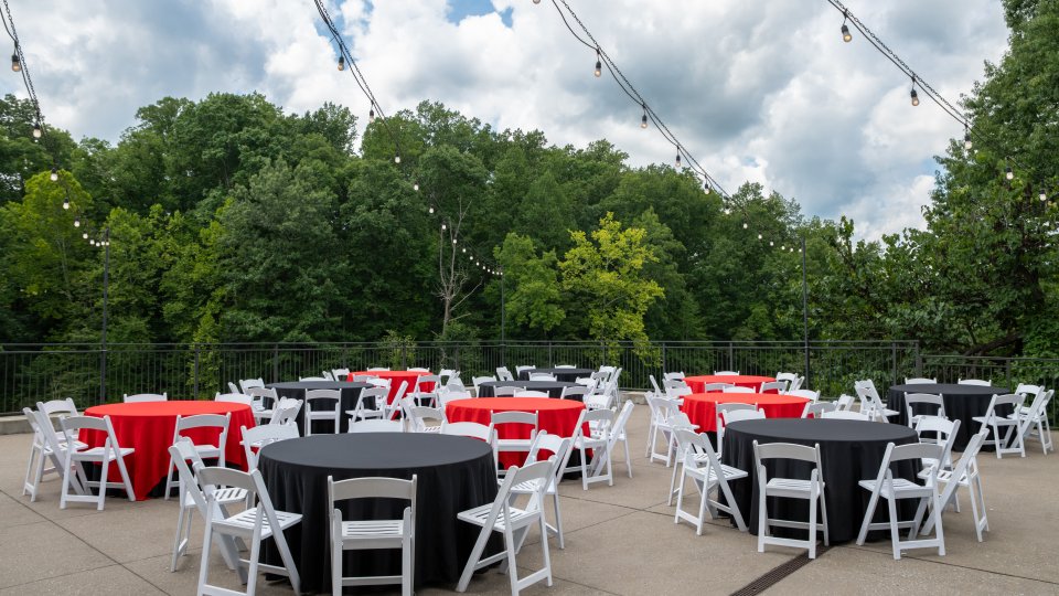 Outdoor event setup with red and white tablecloths and string lights.