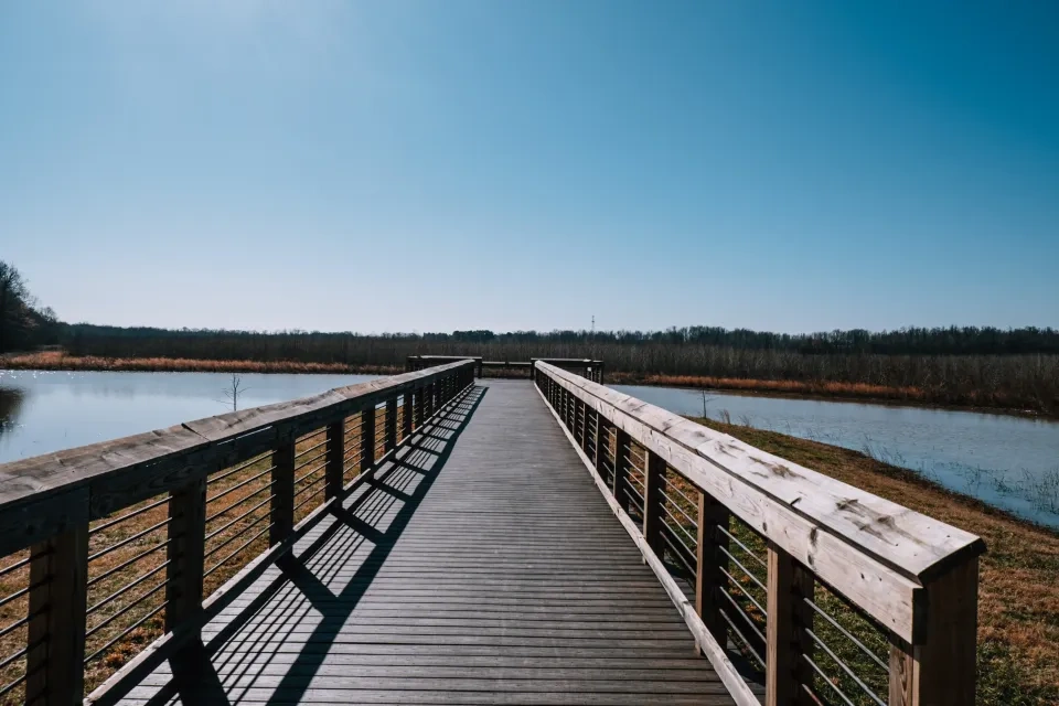 Wooden boardwalk over a river under a clear blue sky.