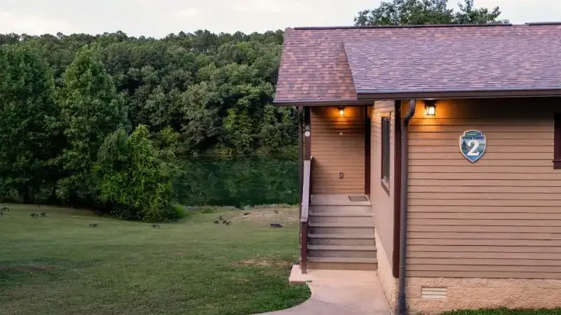 Cabin exterior with steps, surrounded by green trees and a lake in the background.