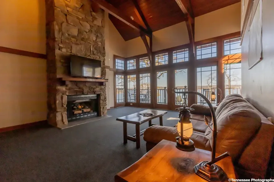 Cozy living room with stone fireplace, large windows, and rustic decor.
