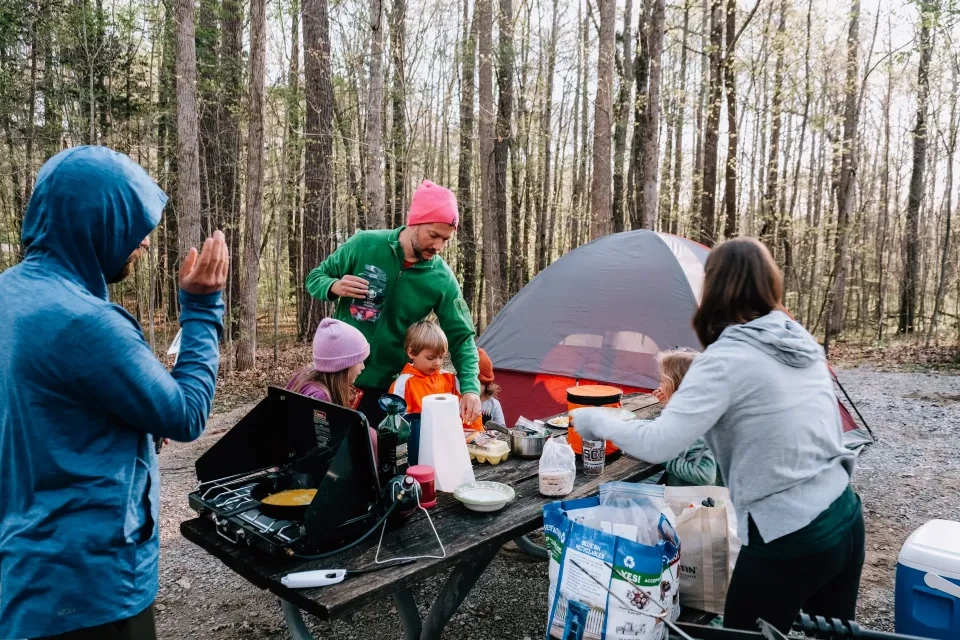 Family cooking at a campsite with a tent and trees in the background.
