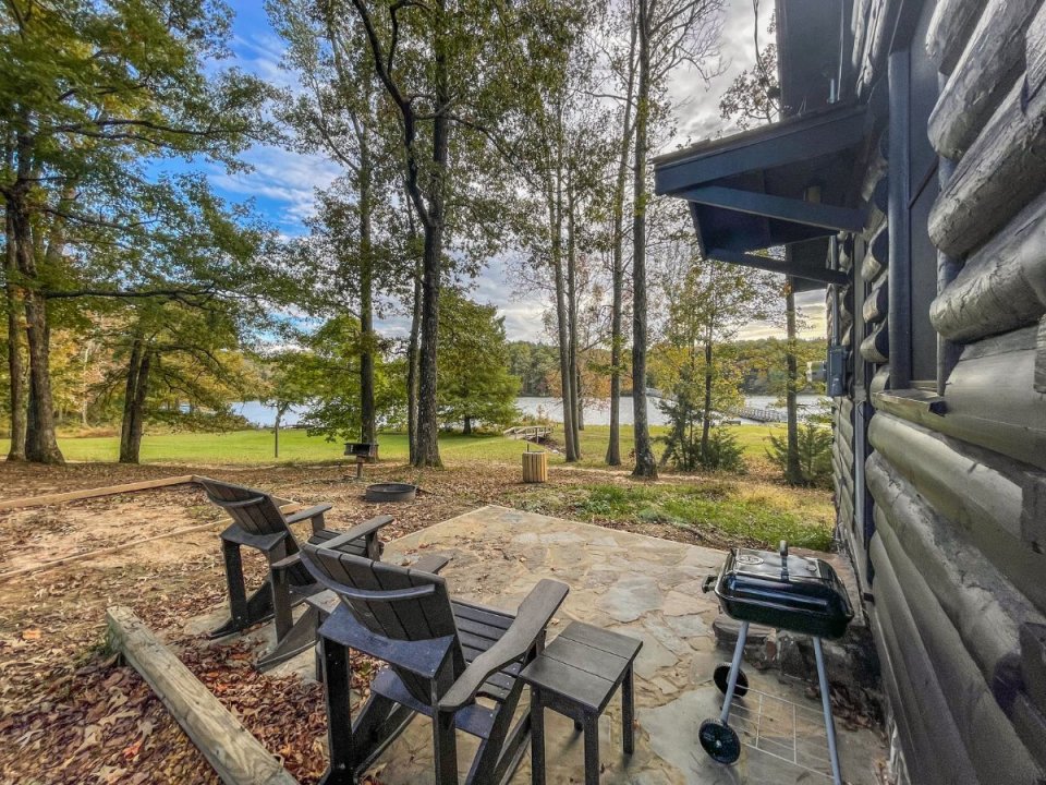 Patio with chairs beside a cabin overlooking a serene lake surrounded by trees.