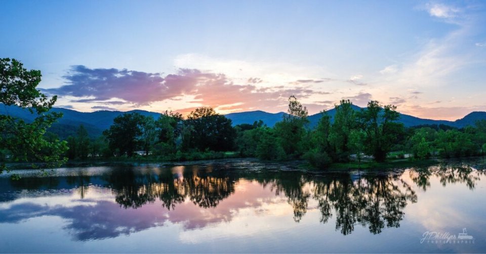 Sunset over a tranquil lake with reflective water and silhouetted trees.