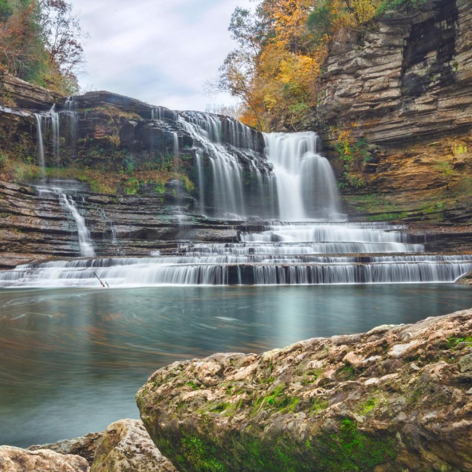 Autumn waterfall cascading over layered rocky cliffs into a serene pool.