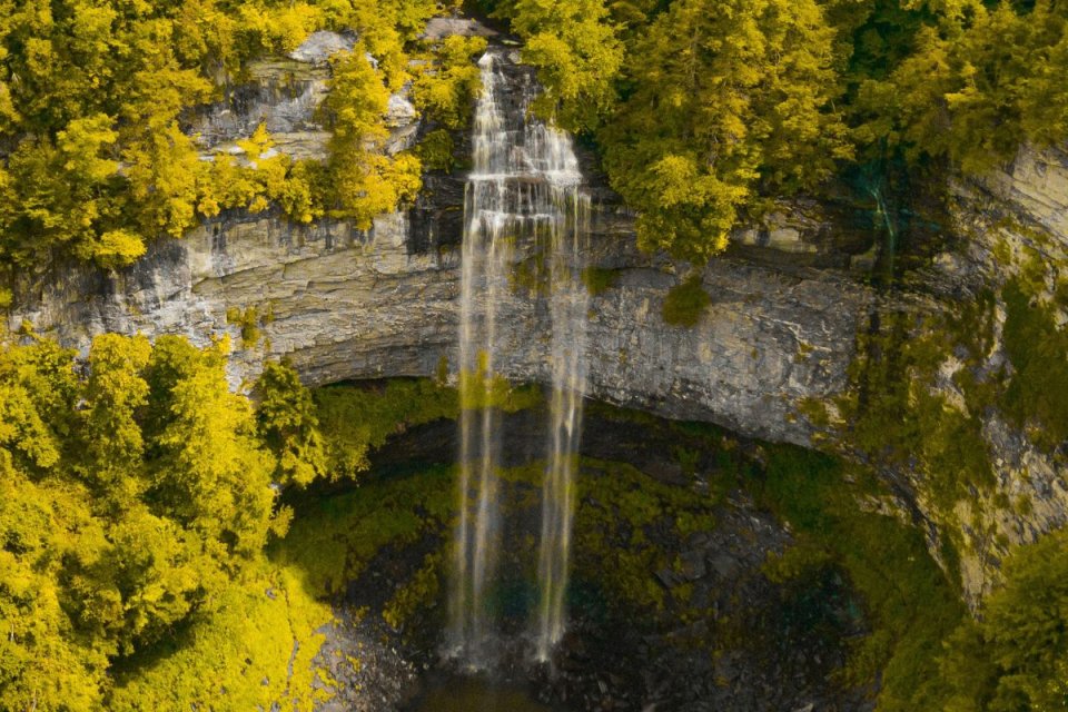 Aerial view of a waterfall cascading over a cliff surrounded by autumn trees.