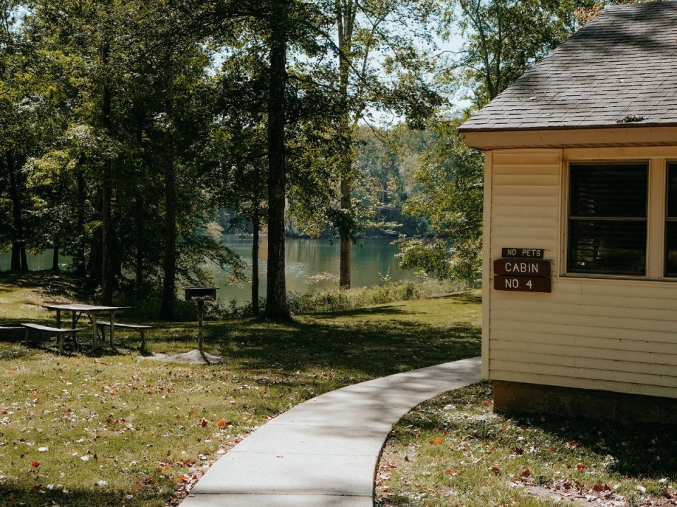 Curved pathway leading to a cabin near a tranquil lake surrounded by trees.