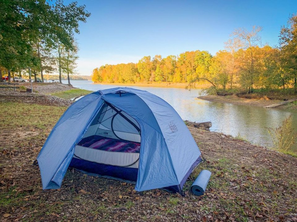 Tent pitched by a serene lakeside with autumn trees in the background.