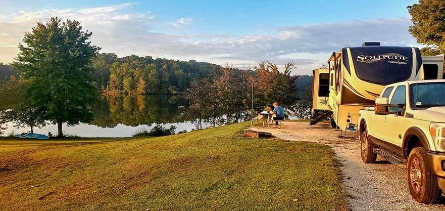 RV parked by a serene lake at sunset, with surrounding trees.