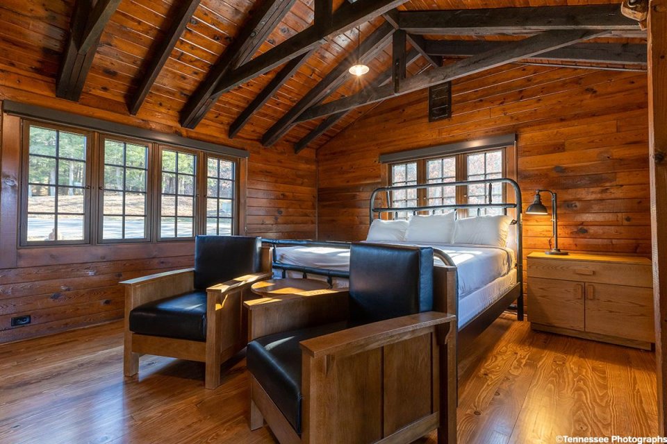 Cozy wooden cabin bedroom with a large bed and two armchairs near the window.