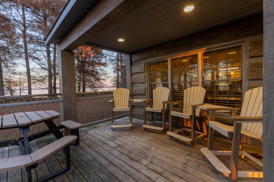 Cozy wooden deck with chairs at sunset, overlooking a lake.