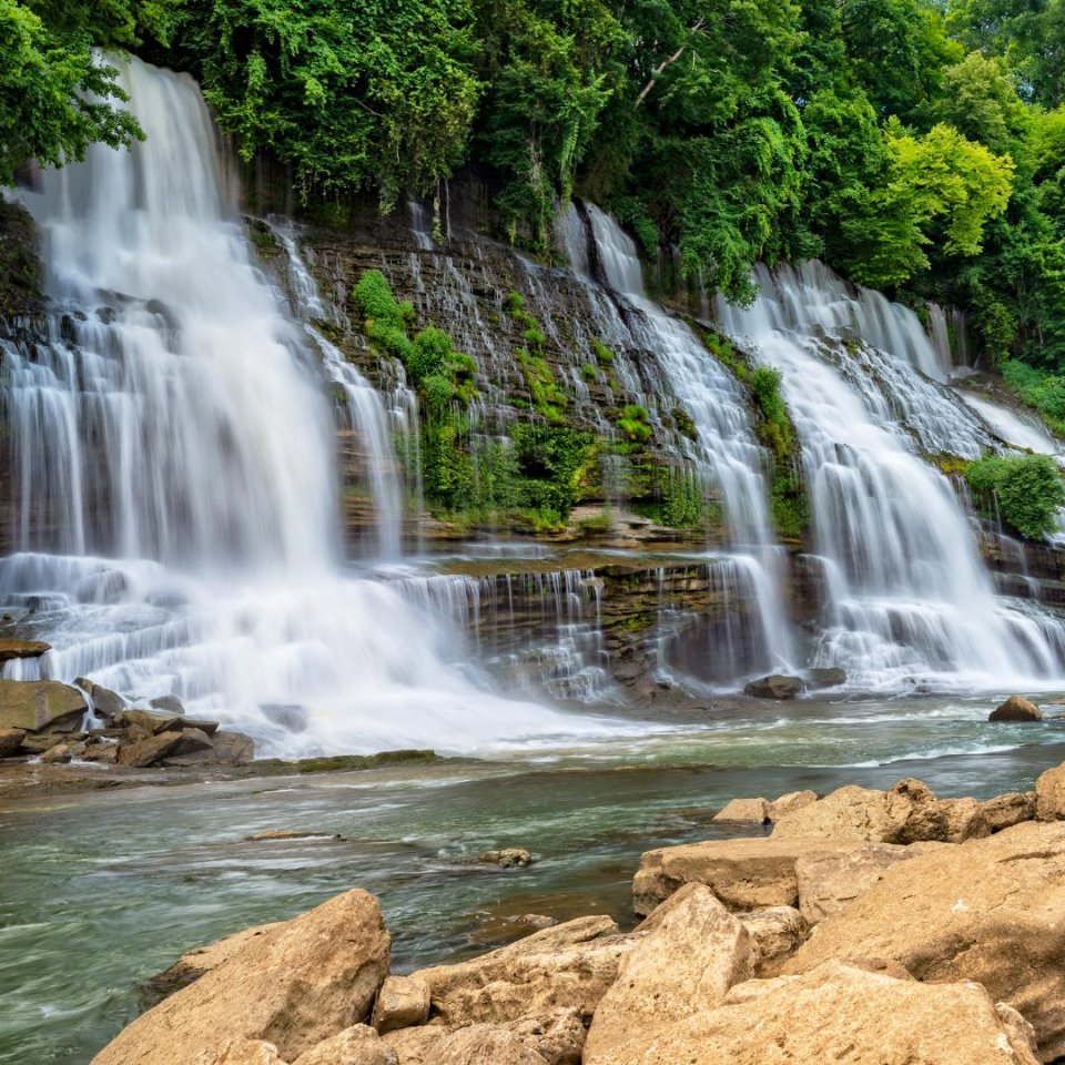 Lush waterfall cascading over rocky ledges into a serene river.