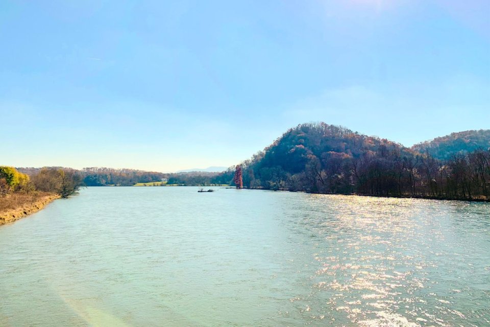 Serene river landscape with a boat and forested hills under a clear sky.