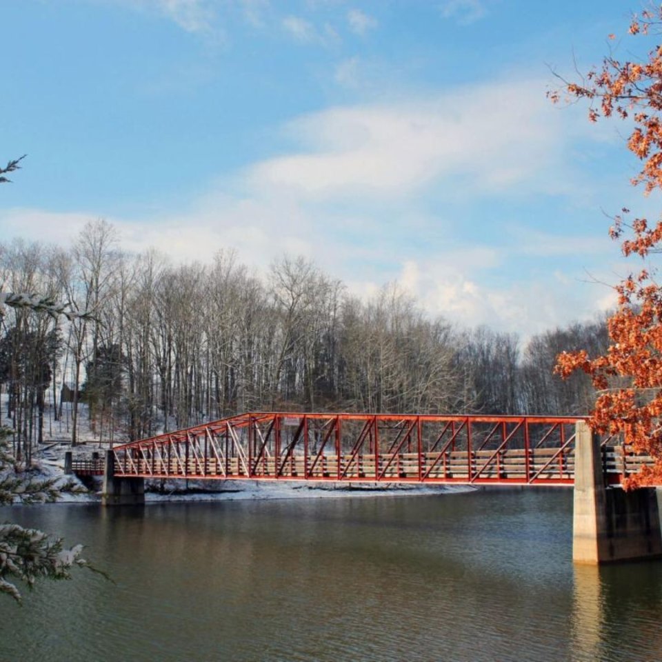 Red bridge over a serene lake surrounded by snowy trees and autumn foliage.