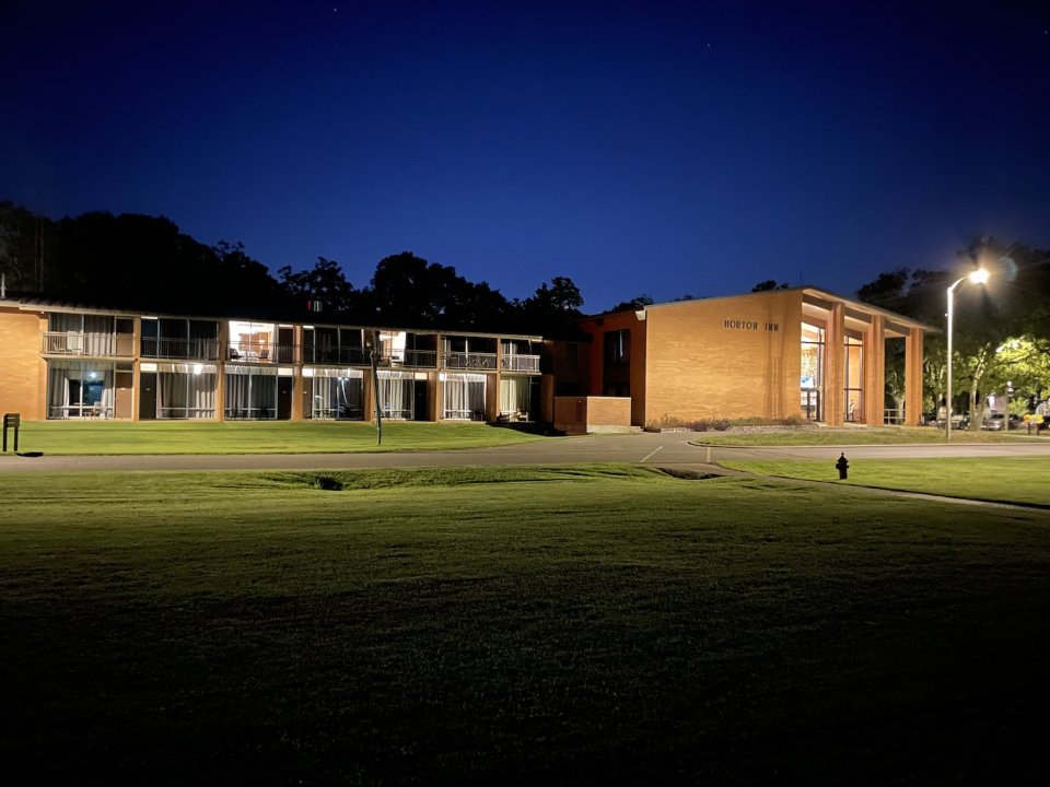 Modern brick building lit at night with surrounding trees.