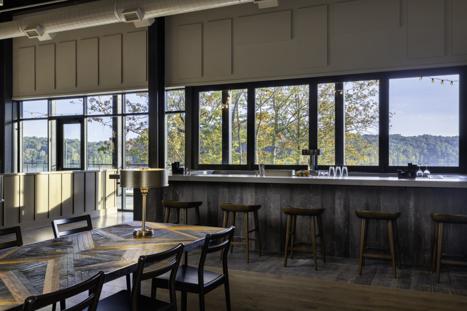 room with a long table and bar area with seating and windows providing natural sunlight