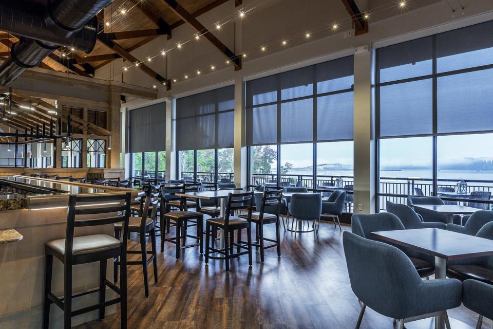 room with large windows, a high ceiling, a bar, several tables, and several chairs