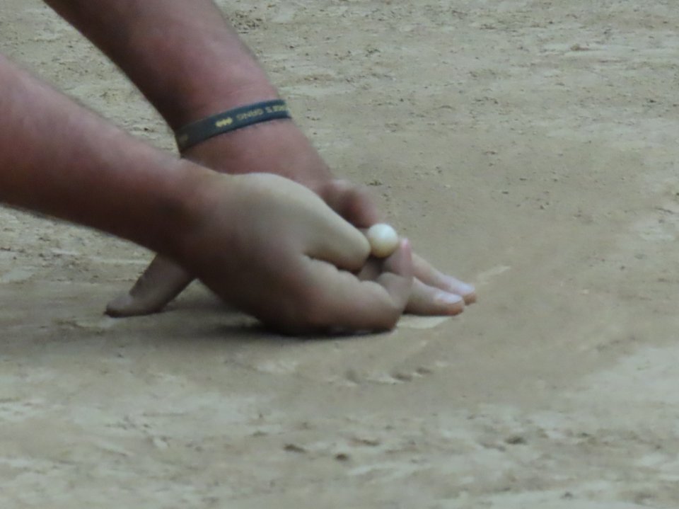 a hand holding a marble, read to flick the marble, while another hand is on the ground