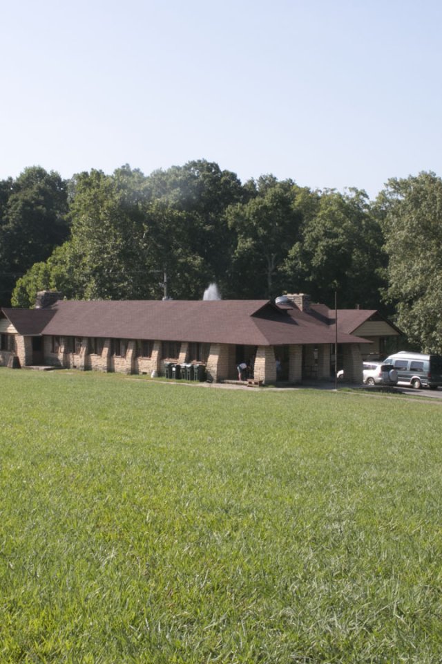 grass field with a large cabin in the distance with parking