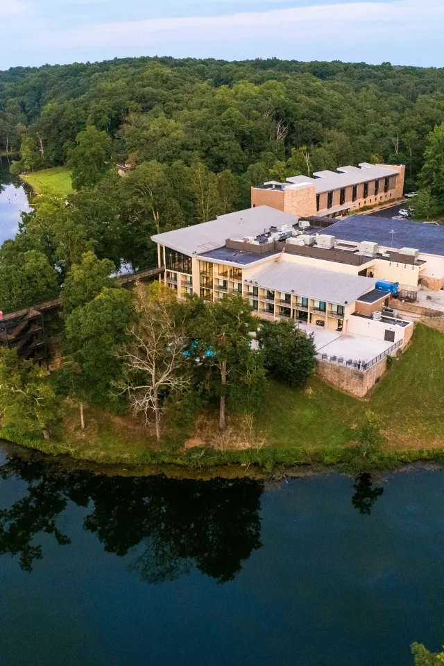 Aerial view of a riverside building surrounded by lush green forest.