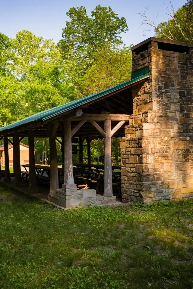 Stone picnic shelter with green roof, set amidst lush trees.