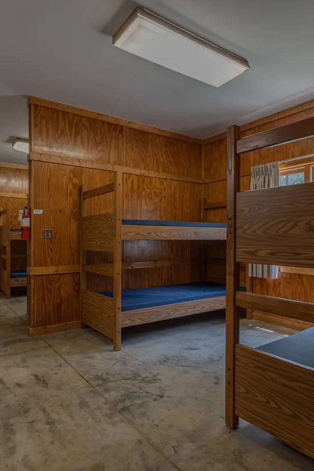 Wooden dorm room with bunk beds, concrete floor, and soft lighting.