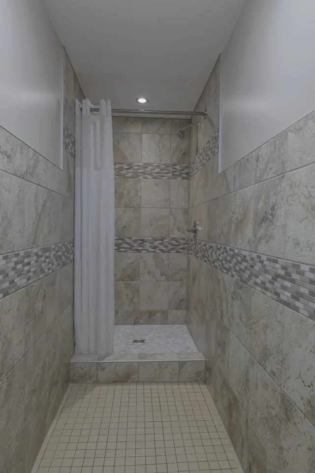 Tiled shower with beige and gray stone, and a white curtain.