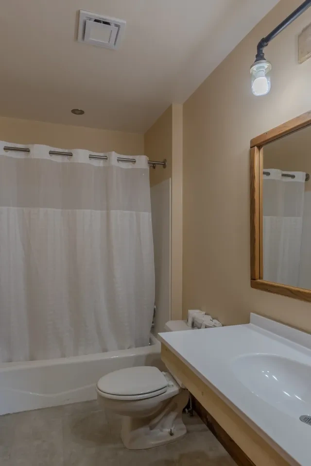 Beige bathroom with a shower, toilet, and sink with a mirror above.