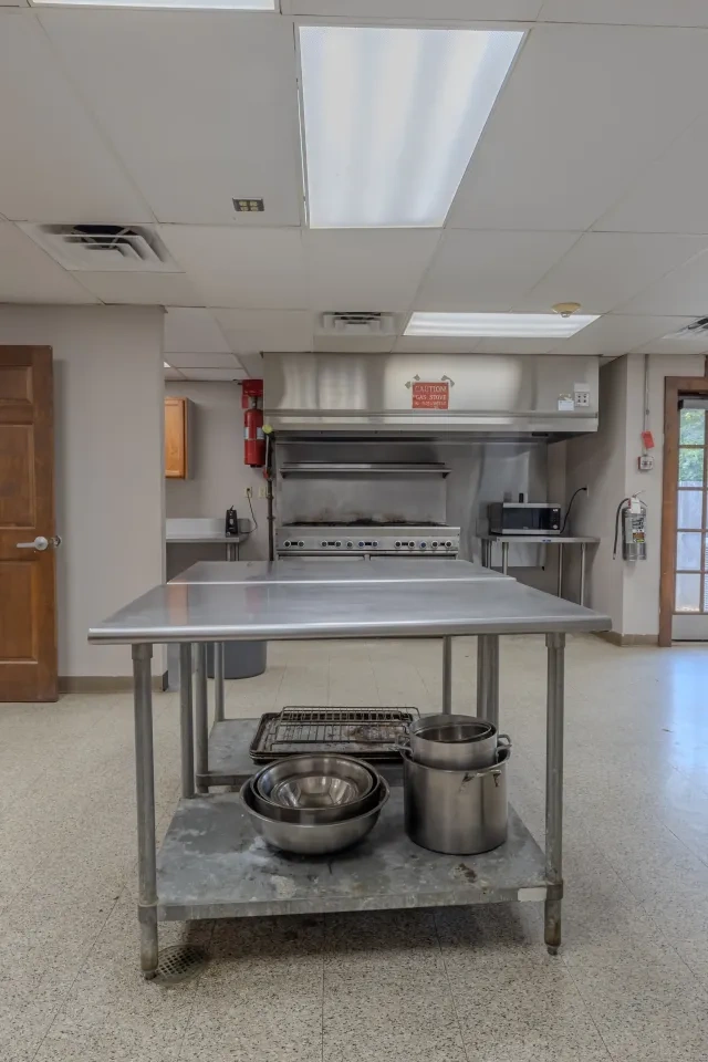 Commercial kitchen with metal island, stove, and sink. Doorway and exit sign visible.