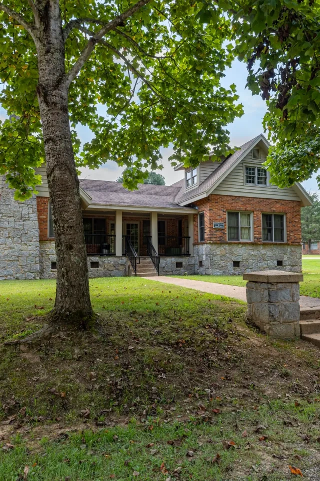 Brick house with stone accents, surrounded by trees, sunny day.