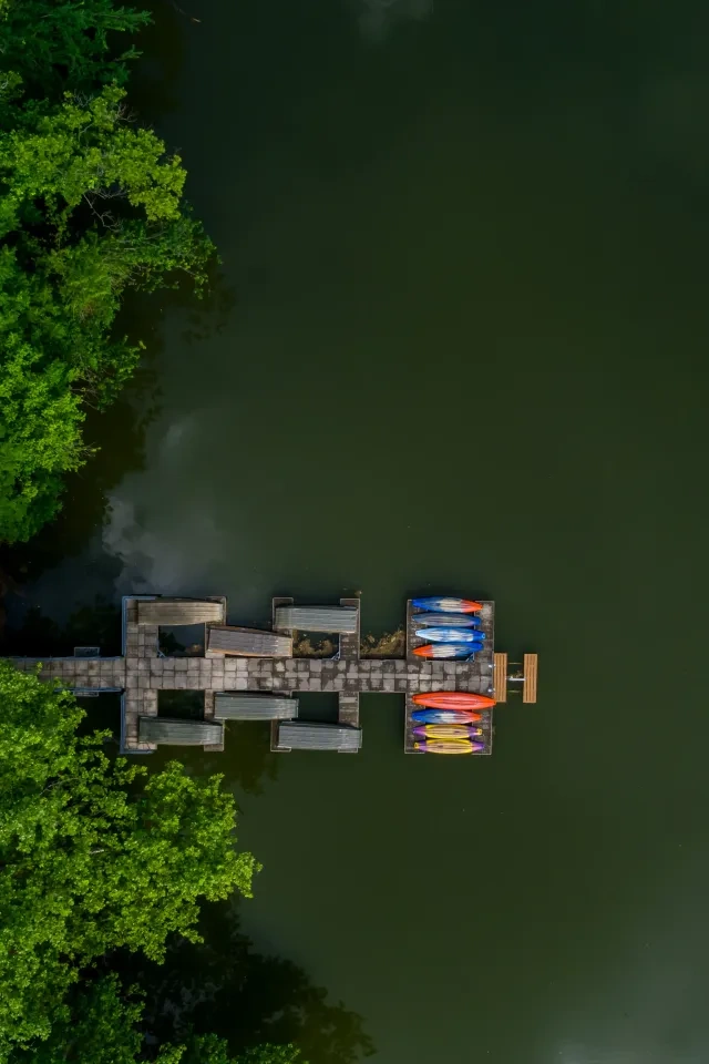 Kayaks on dock by lush green trees and dark water.