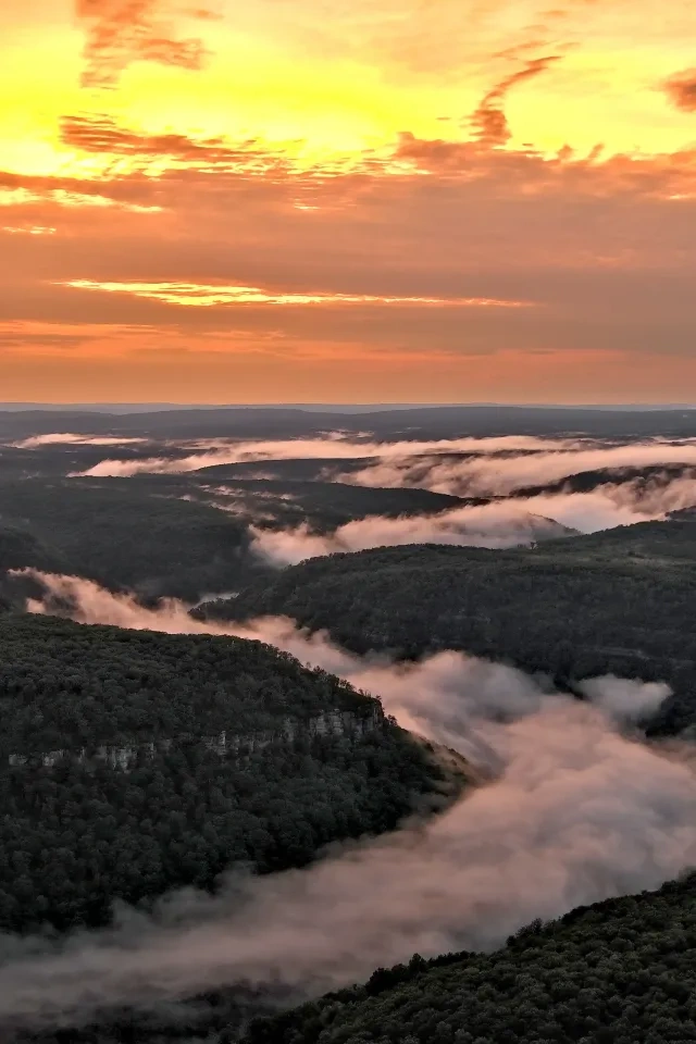 Sunset over hills with clouds and mist in valleys.