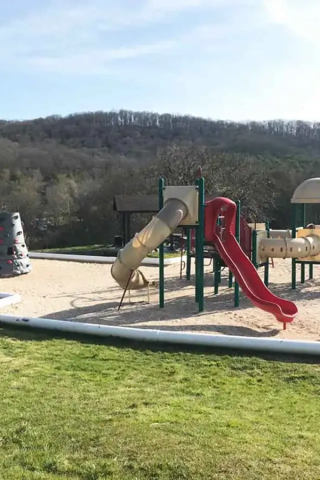 Playground with slides and climbing structures surrounded by scenic hills.