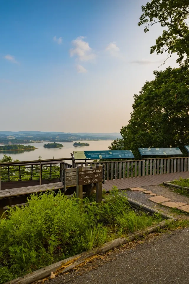 Scenic lake view from overlook deck with trees and informational signs.