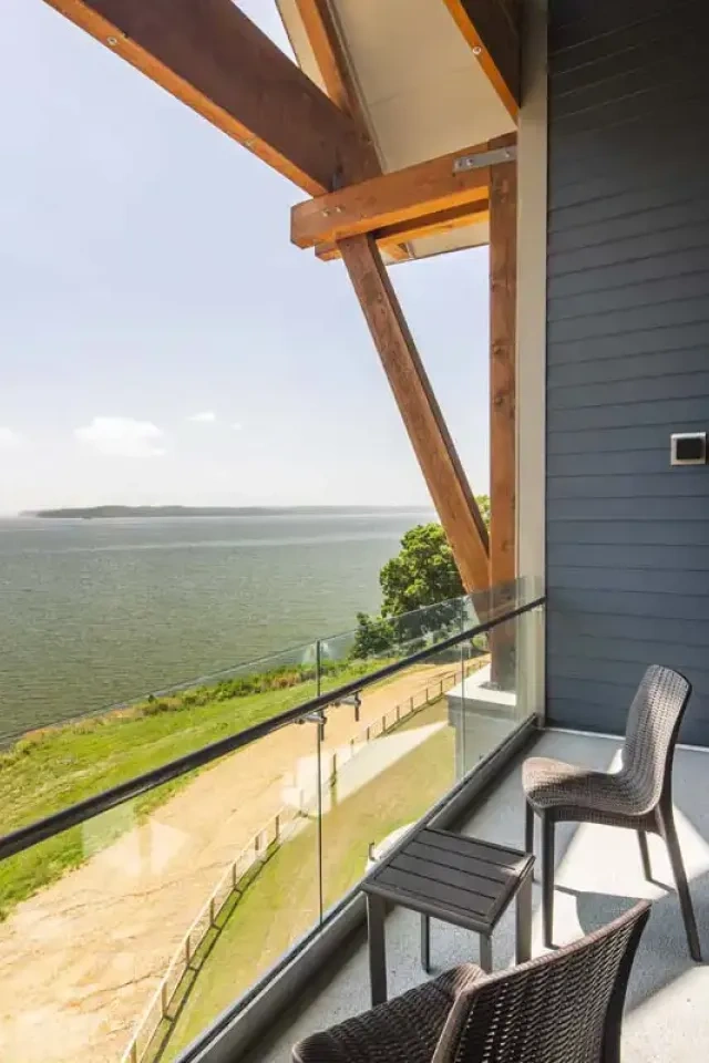 Balcony with chairs, overlooking a serene lake and greenery, under a clear sky.