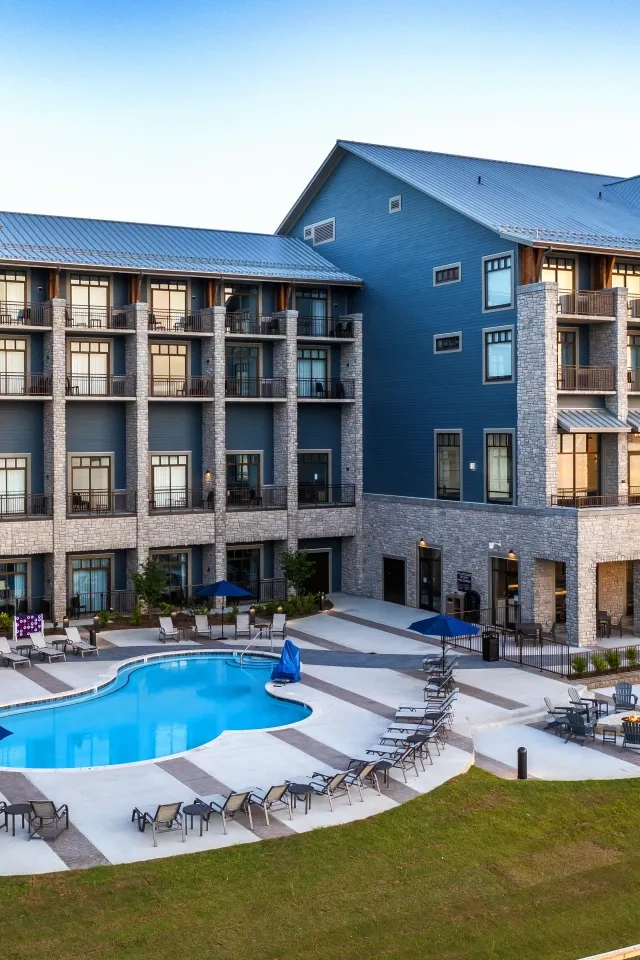 Hotel with balconies and a pool, surrounded by chairs and umbrellas.