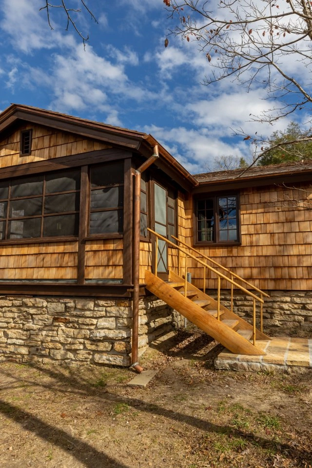 Wooden cabin with stone foundation, surrounded by trees and a bright blue sky.