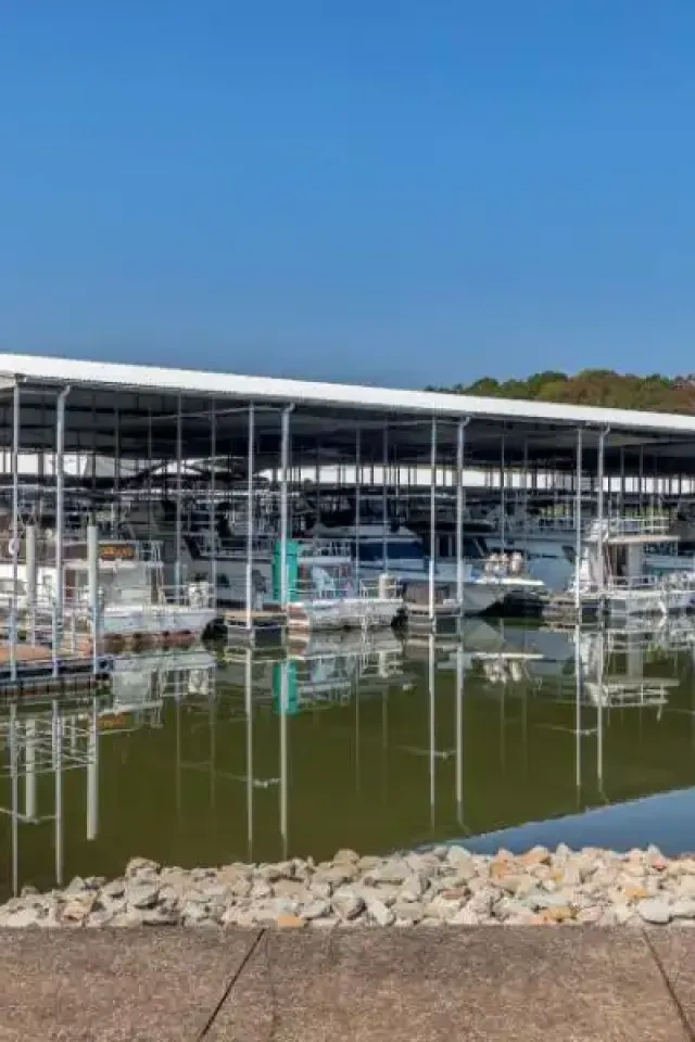 Marina with docked boats and a covered roof reflecting on still water.
